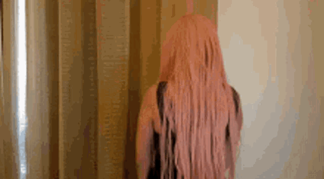 a woman with long pink hair is standing in front of a window .
