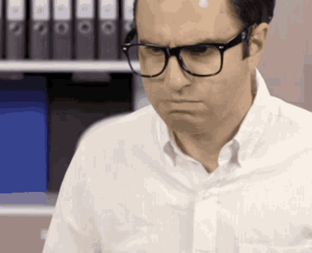 a man wearing glasses and a white shirt is looking down