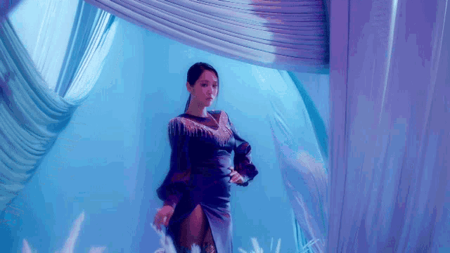 a woman in a purple dress is standing in front of a purple curtain