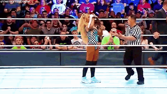 a woman is standing in a wrestling ring while a referee looks on .