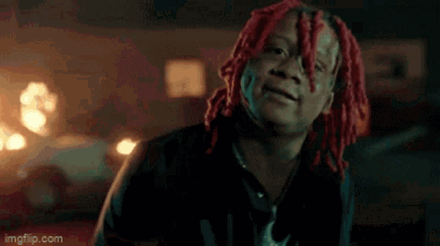 a man with red dreadlocks is making a funny face while looking at the camera .