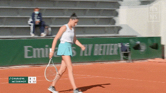 a woman holding a tennis racquet on a court with emirates fly better written on a green wall behind her