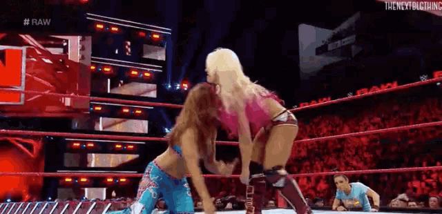 two women are wrestling in a wrestling ring while a man watches .