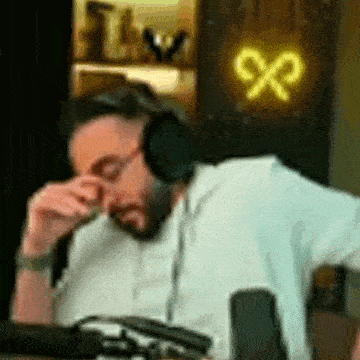 a man wearing headphones is sitting in front of a microphone and covering his eyes .