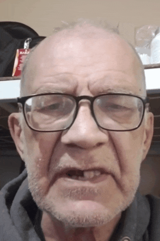 a man with glasses and a beard looks at the camera with a bag of red bull in the background