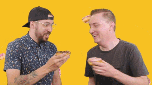 two men eating donuts on a yellow background with donuts falling around them