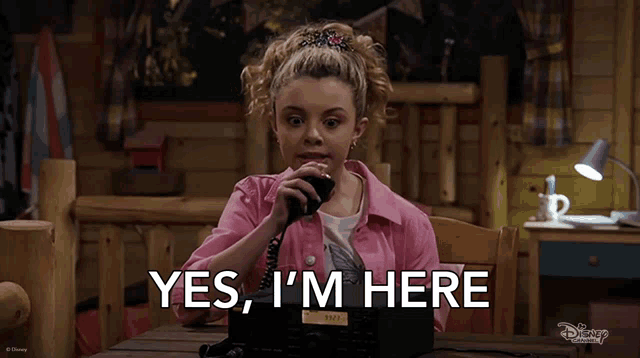 a girl in a pink jacket is talking on a telephone and the words yes i 'm here are on the screen