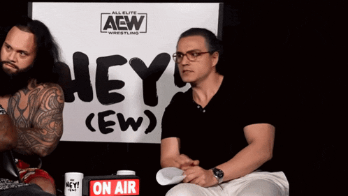 two men sit in front of a sign that says hey ew