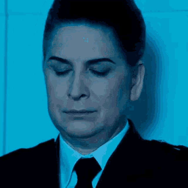 a woman in a suit and tie is standing in front of a wall with her eyes closed .