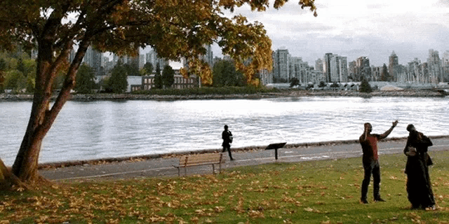 a couple standing in a park near a body of water with a city in the background