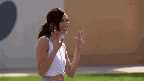 a woman in a white crop top and blue shorts is waving her hands .