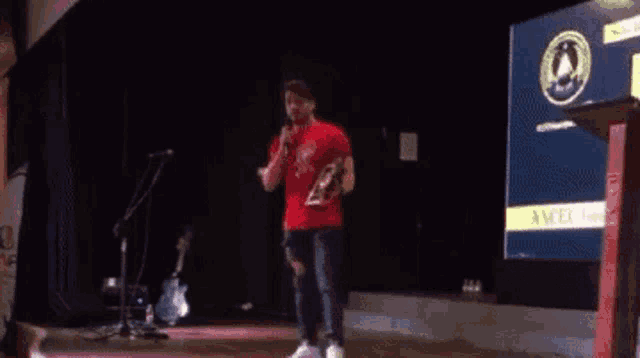 a man in a red shirt is standing on a stage with a microphone in his hand