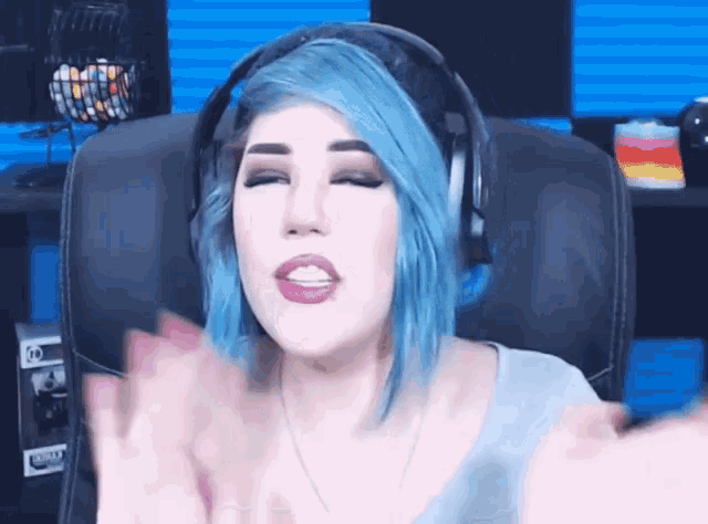 a woman with blue hair wearing headphones is clapping her hands