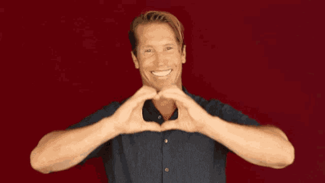 a man is making a heart shape with his hands and smiling .