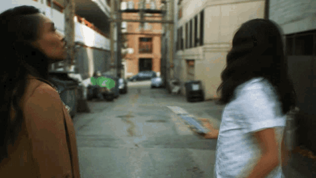 two women are standing in a narrow alleyway looking at something