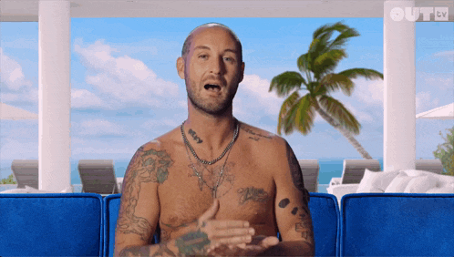 a shirtless man with tattoos on his chest is sitting on a blue couch in front of a palm tree and the words out tv behind him