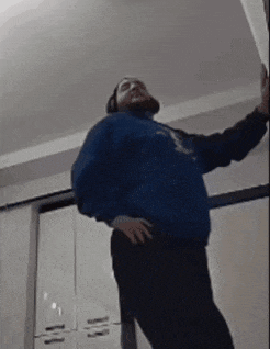 a man in a blue sweatshirt and black pants is standing in a kitchen .