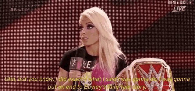 a woman is talking into a microphone while holding a wwe championship ring .