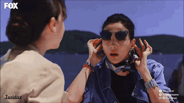 a woman wearing sunglasses talks to another woman with the fox logo on the bottom