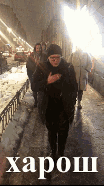 a group of people are walking down a snowy street with the word " harosh " on the bottom right