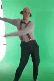 a bald man in suspenders and a bow tie is dancing in front of a green screen .