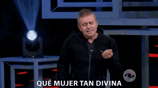 a man in a black jacket is standing in front of a sign that says " que mujer tan divina "