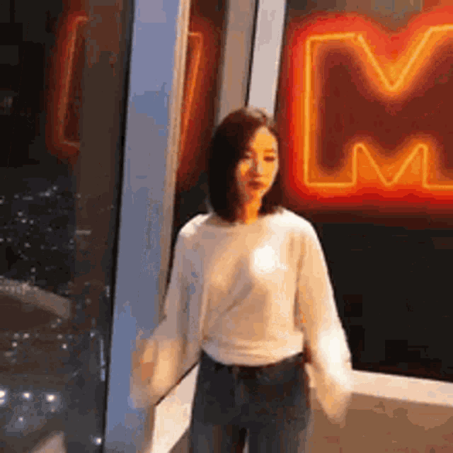 a woman is standing in front of a neon sign that says m