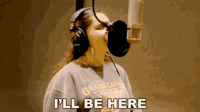 a woman wearing headphones is singing into a microphone and says i 'll be here