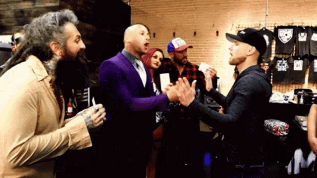 a group of men are standing in a room and one of them is wearing a purple suit .