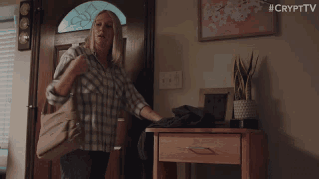 a woman in a plaid shirt is standing in front of a door holding a bag