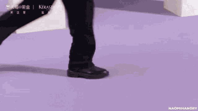 a person wearing black shoes is walking on a purple floor .