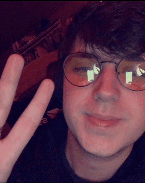 a young man wearing glasses and headphones giving the peace sign