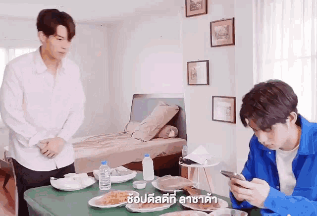 two men are sitting at a table with food and one is looking at his phone