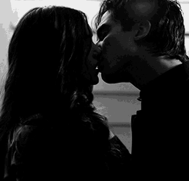 a black and white photo of a man and a woman kissing .