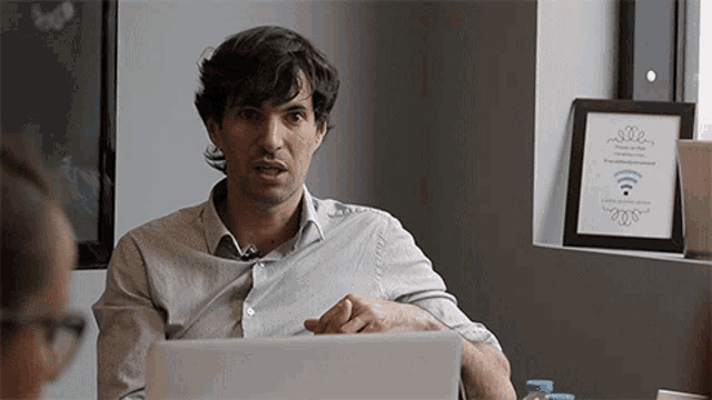 a man sitting at a table with a laptop and a picture on the wall that says " wifi "