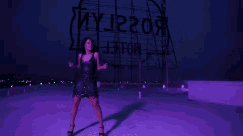 a woman is dancing on a rooftop in front of a large billboard .