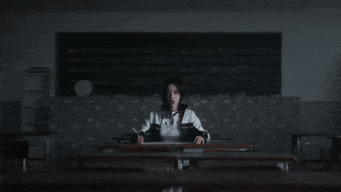 a girl sits at a desk in front of a blackboard that says ' i 'm sorry '