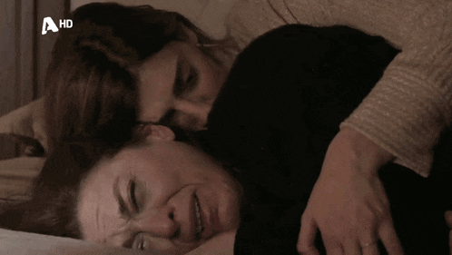 two women laying on a bed with a hd logo on the bottom right