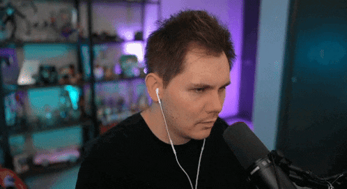 a man wearing ear buds stands in front of a black microphone