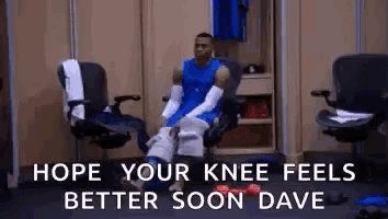 a basketball player is sitting in a chair in a locker room with his knee wrapped in bandages .