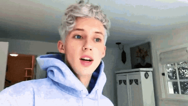 a young man with white hair and blue eyes is wearing a blue hoodie in a living room .