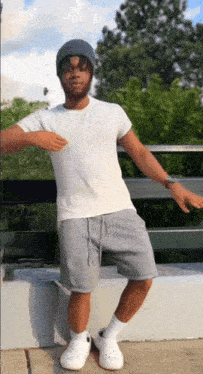 a man wearing a white shirt and grey shorts is standing on a ledge with his arms outstretched