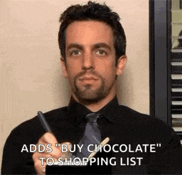 a man in a black shirt and tie is holding a pen and saying `` buy chocolate '' to shopping list .