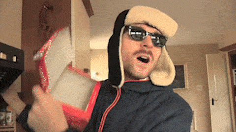 a man wearing a furry hat and sunglasses is holding a red box