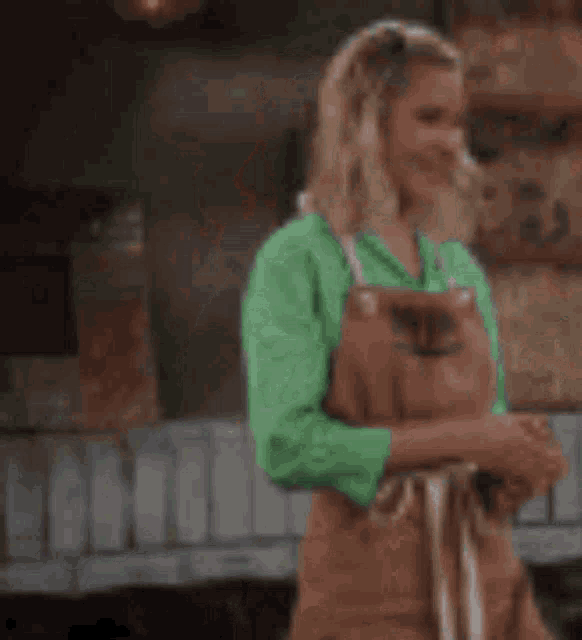 a woman in a green sweater and apron is standing in front of a wooden bench .