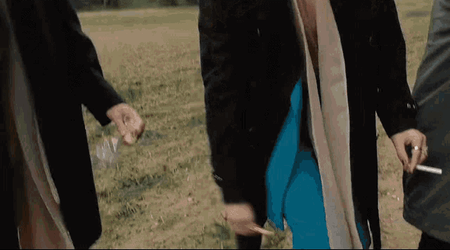 a group of people are standing in a field holding hands and one of them is holding a cigarette .
