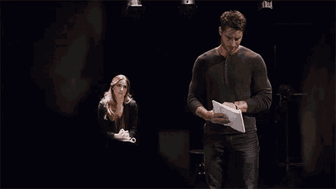 a woman is sitting in front of a man in a dark room and looking at him .
