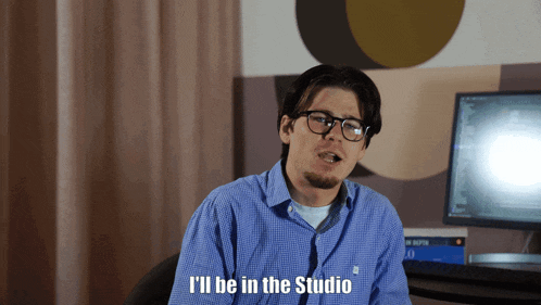 a man wearing glasses and a blue shirt says " i 'll be in the studio "
