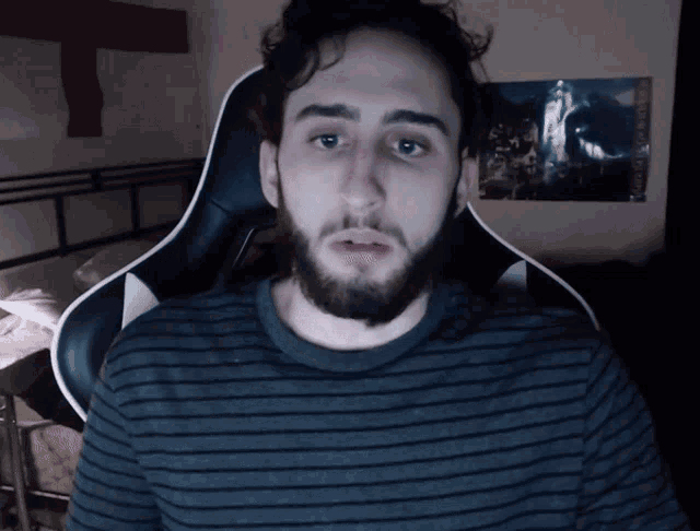 a man with a beard wearing a striped shirt is sitting in a gaming chair