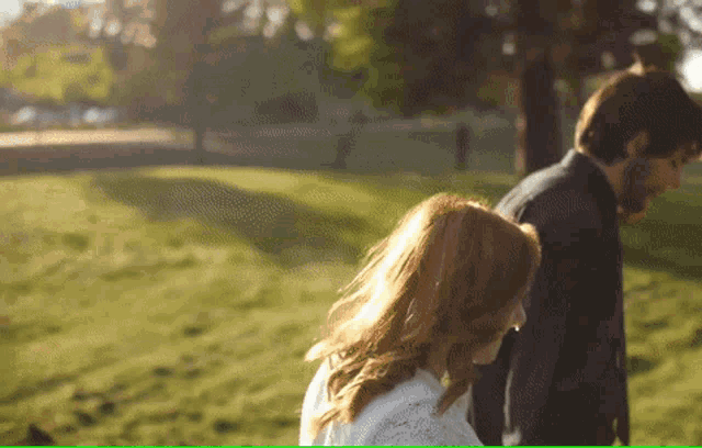 a man and a woman are walking in a park holding hands